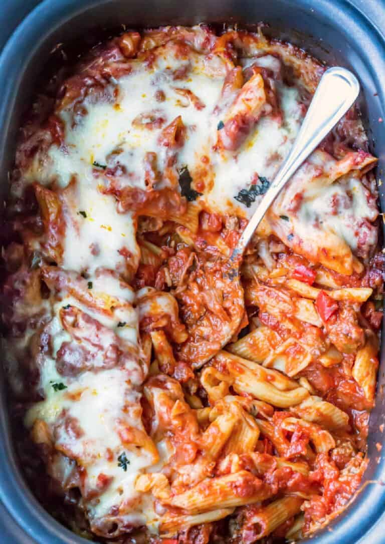 baked ziti in a slow cooker with a spoon in the middle.