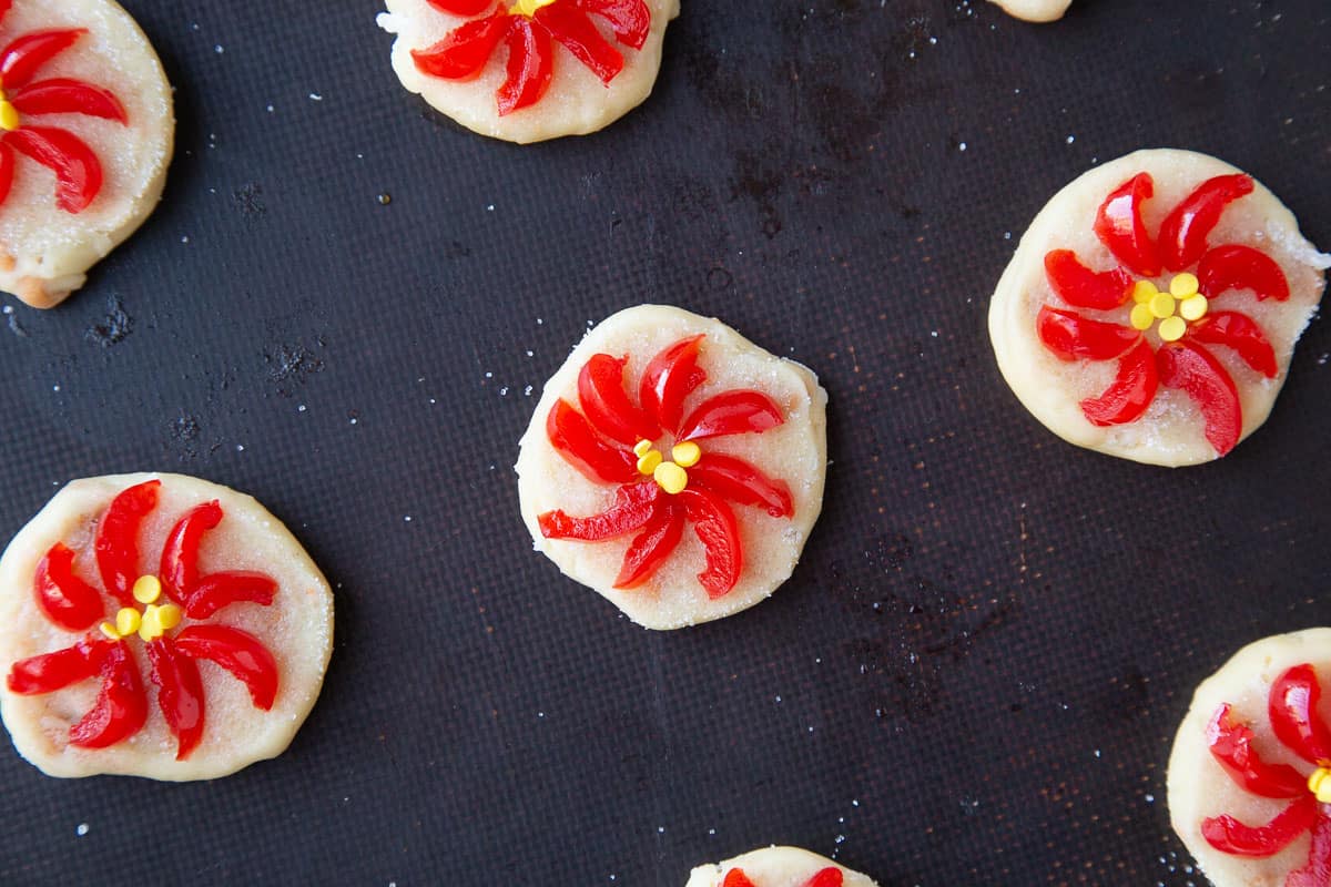 unbaked poinsettia cookies topped with sliced maraschino cherries on a baking sheet.