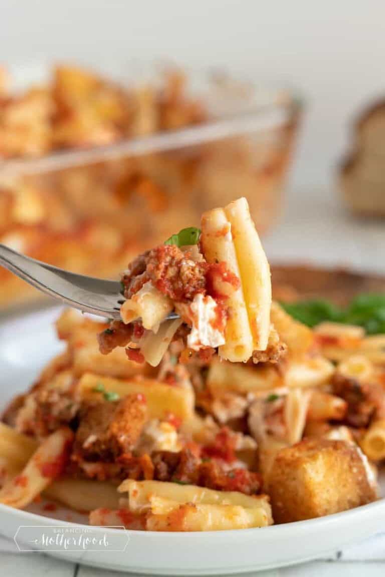 a fork holding several pieces of baked ziti, over a full plate.