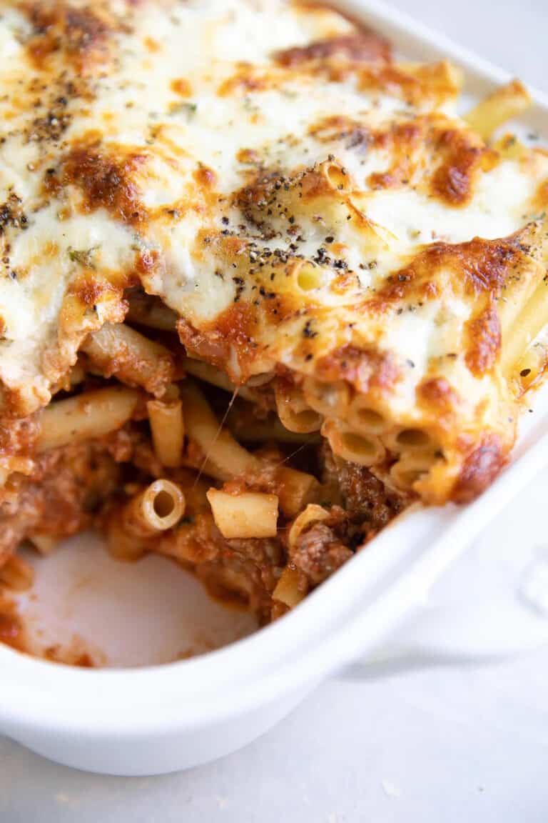 baked ziti in a white casserole dish with a scoop taken out.