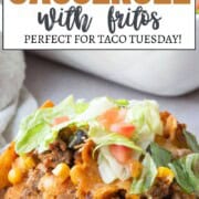 scoop of casserole with ground beef, fritos, and corn, topped with lettuce and diced tomatoes.