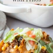 portion of taco casserole on a white plate, topped with lettuce and tomatoes.