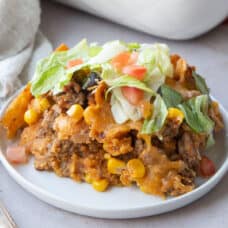 taco casserole with fritos on a small white plate, topped with lettuce and tomato.