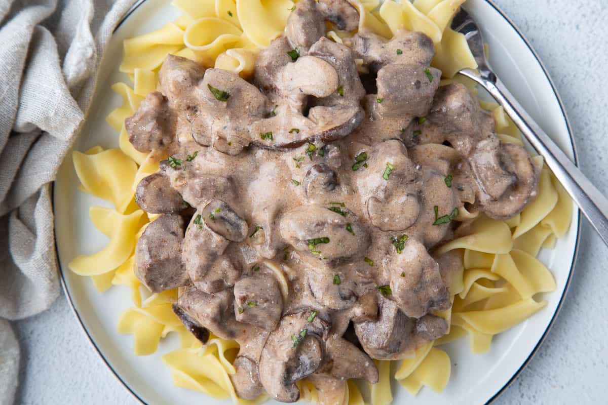 creamy beef stroganoff over egg noodles on a white plate.