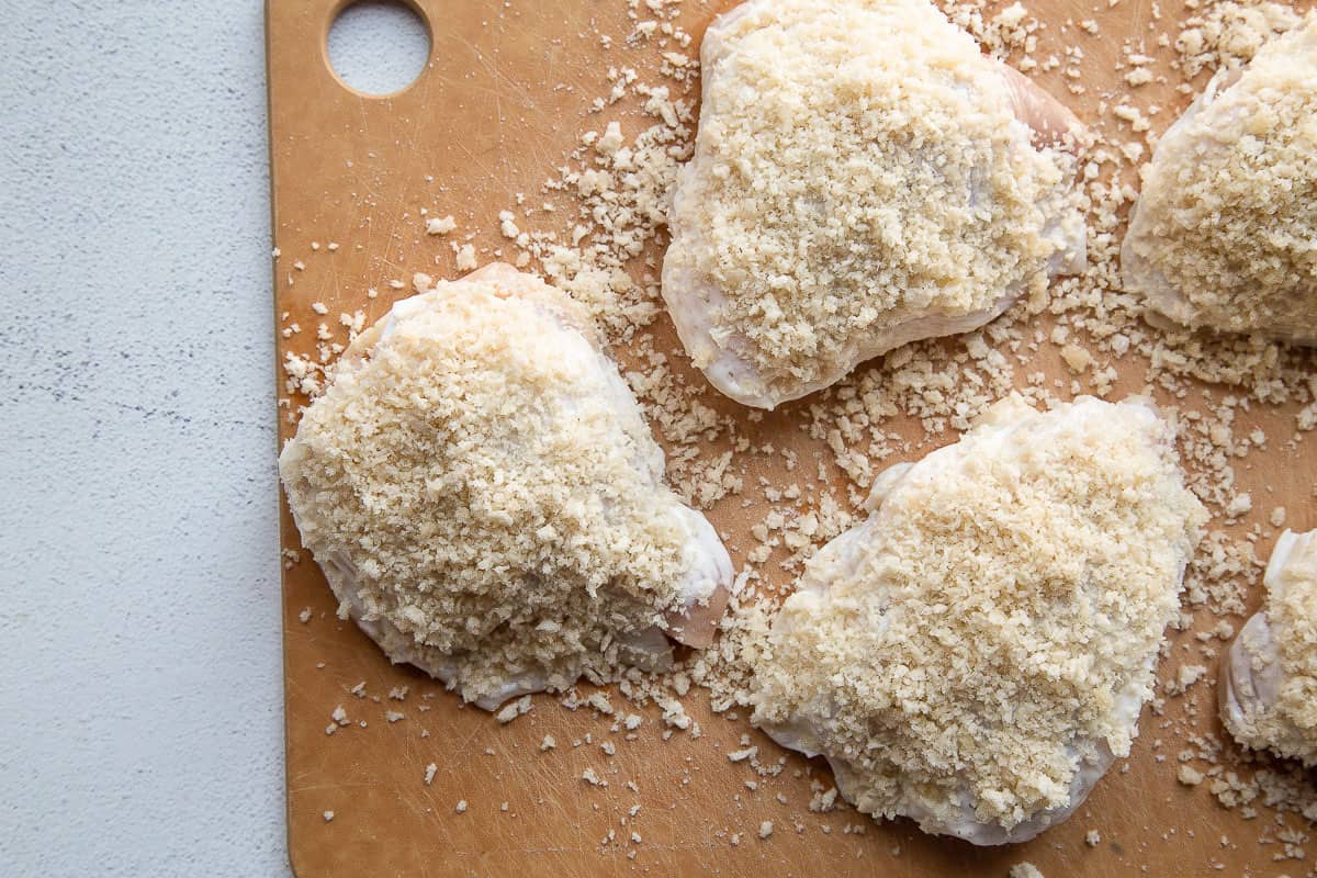 chicken thighs topped with breadcrumbs on a wooden cutting board.
