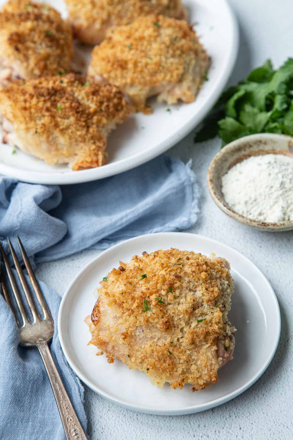 ranch chicken thigh on a white plate, next to a plate of additional breadcrumb topped chicken thighs.