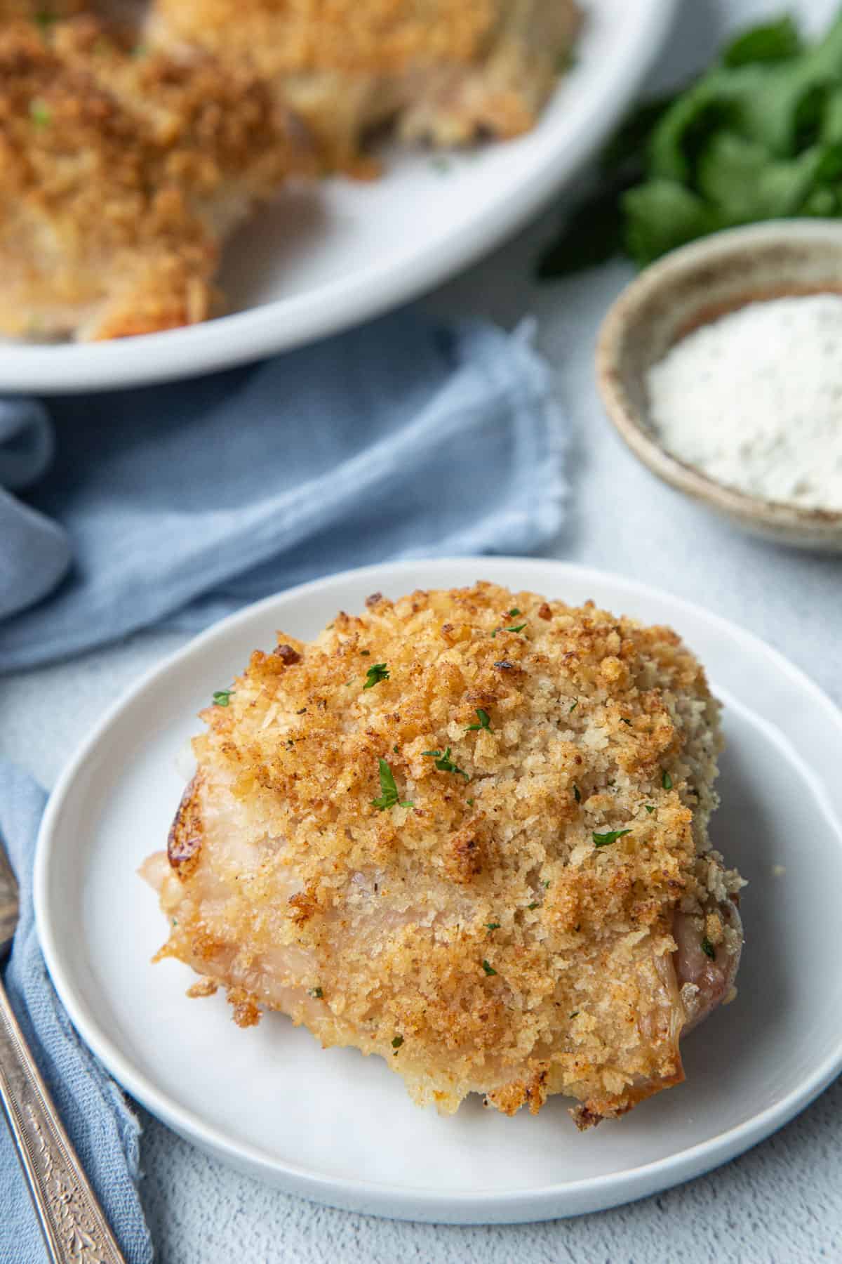 ranch chicken thigh on a white plate, next to a platter of more chicken thighs.