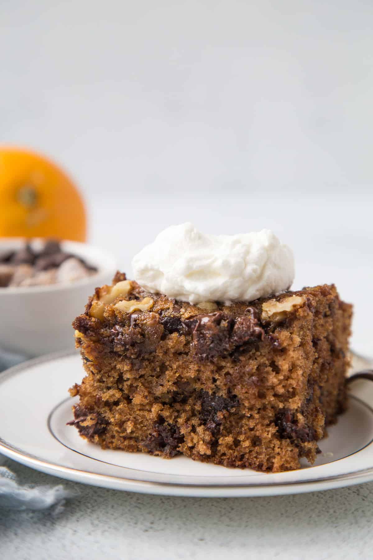 slice of old fashioned date cake with a dollop of whipped cream on top, sitting on a white plate.