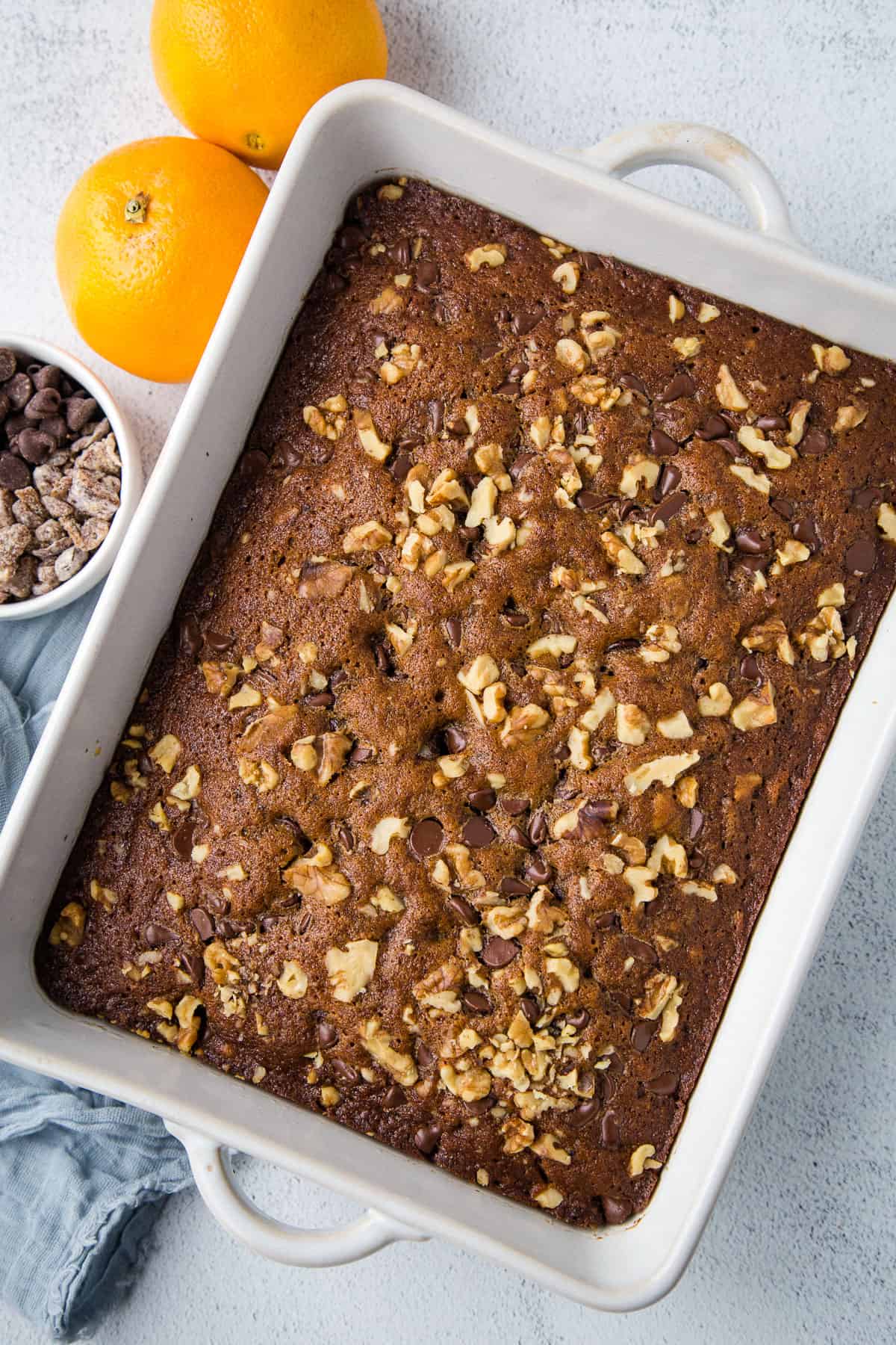 pan of old fashioned date cake in a white dish, topped with chopped nuts and chocolate chips.