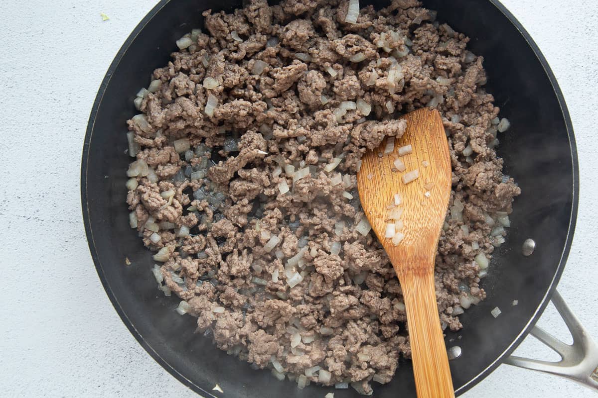 ground beef, onions, and a wooden spoon in a large black skillet.