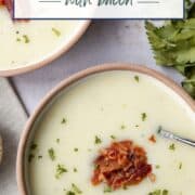 bowl of old fashioned potato soup with a spoon, topped with bacon and chopped parsley.