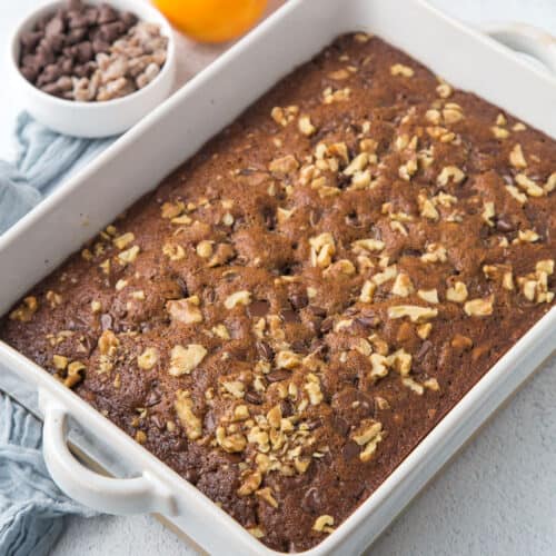 old fashioned date cake topped with walnuts in a white casserole dish.