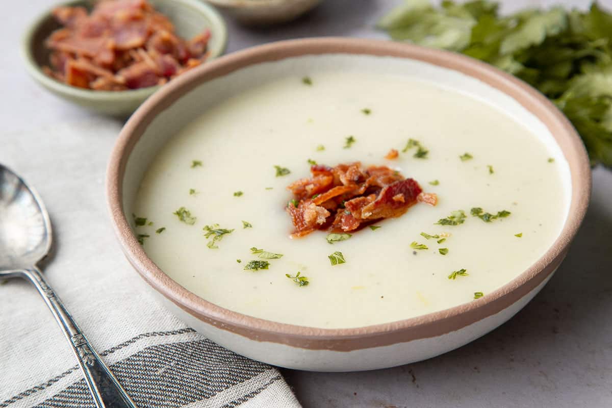 old fashioned potato soup in a beige bowl, topped with crumbled bacon and chopped parsley.