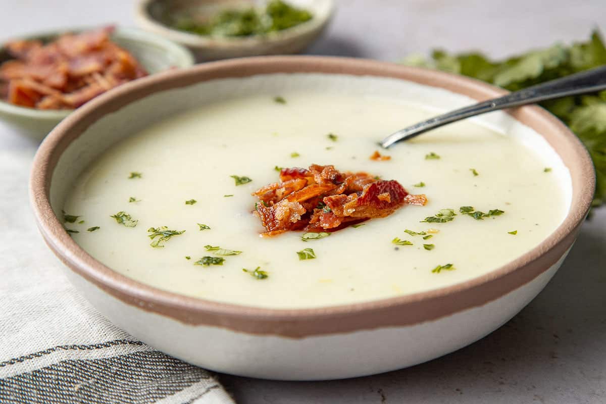 bowl of old fashioned potato soup with a spoon, topped with bacon and chopped parsley.