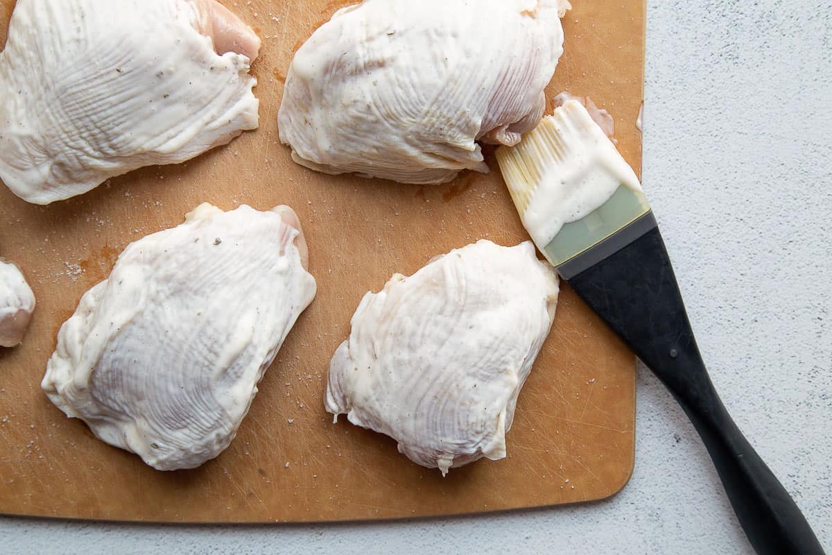 chicken thighs brushed with ranch dressing on a cutting board.