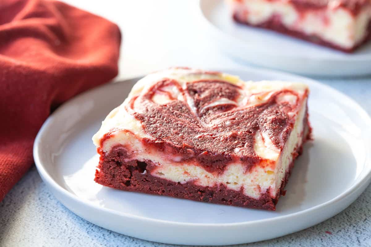 a single red velvet brownie on a white plate next to a red napkin.