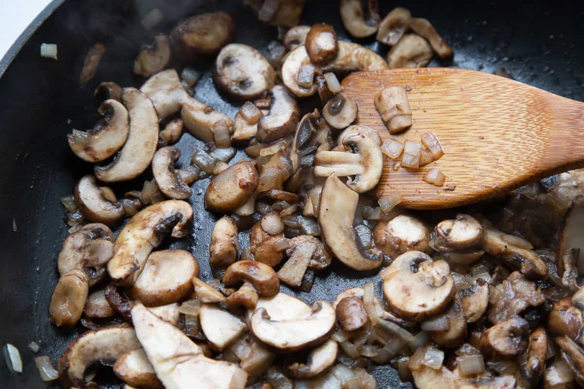 sautéed mushrooms and onions in a skillet with a wooden spoon.