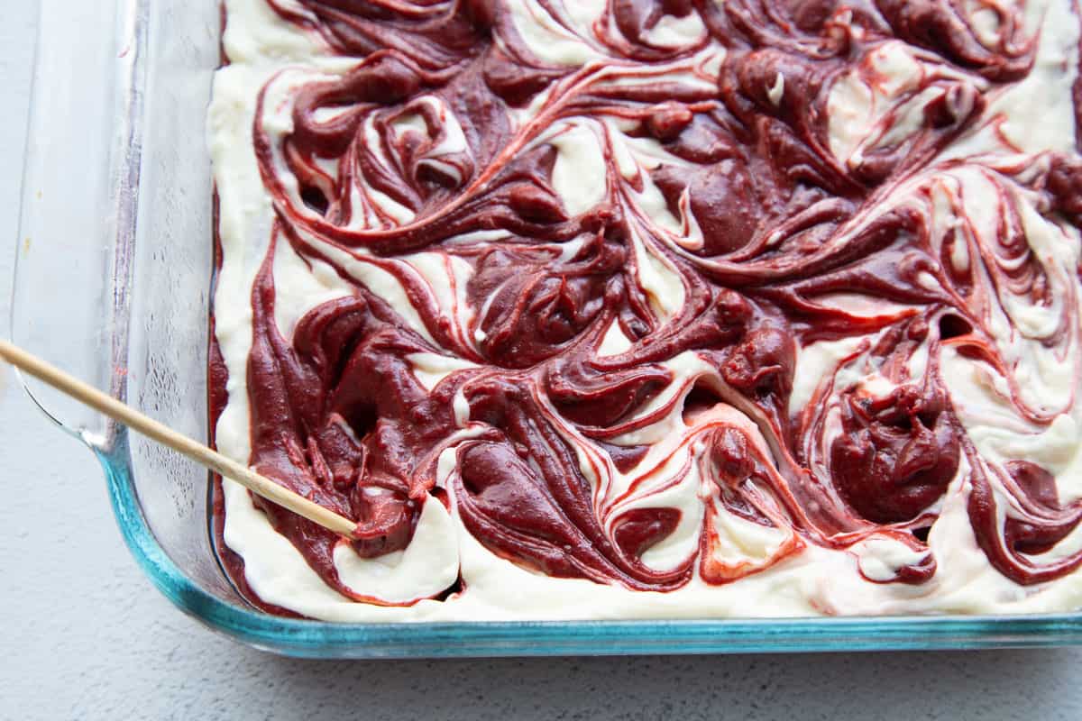 skewer swirling brownie batter and a cream cheese mixture in a glass baking dish.