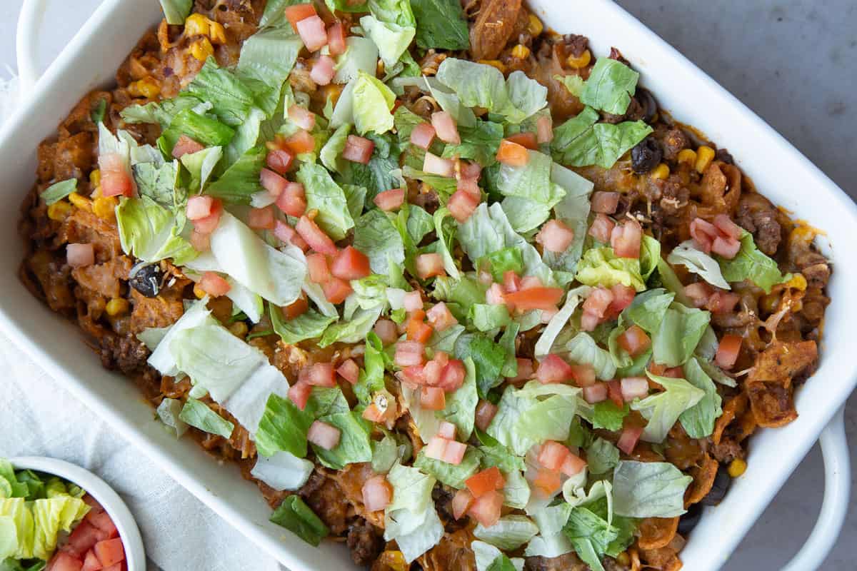 taco casserole topped with lettuce and tomato in a white casserole dish.