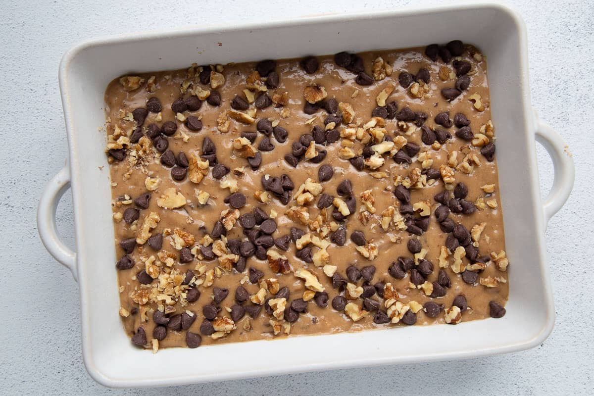 unbaked date cake batter in a white 13x9 inch cake pan, topped with chocolate chips and walnuts.