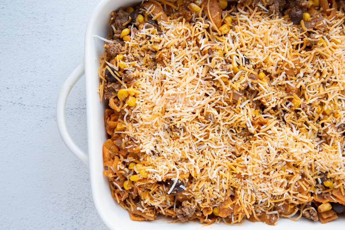 unbaked taco casserole topped with shredded cheese in a white casserole dish.