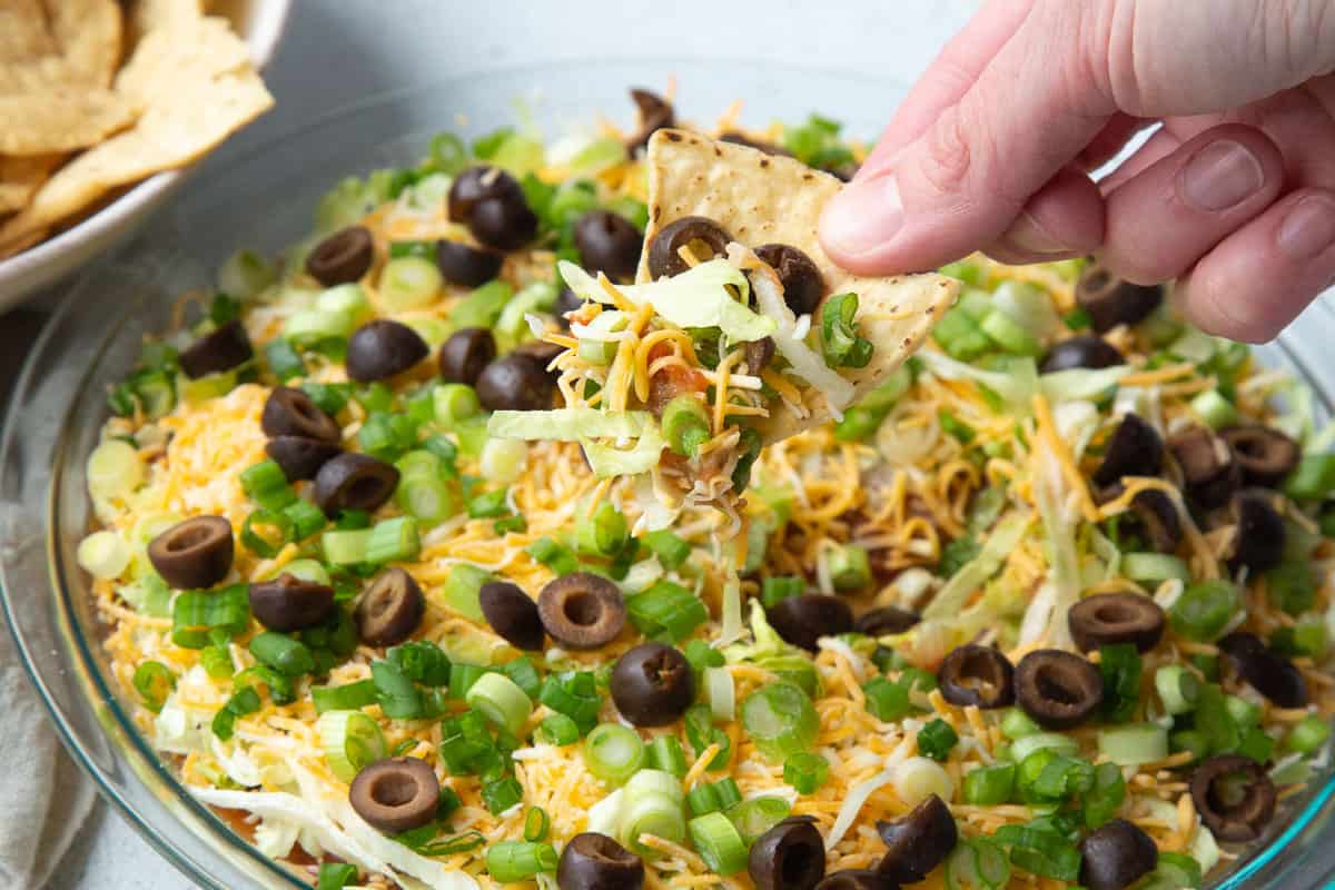 hand holding a tortilla chip filled with layered taco dip.