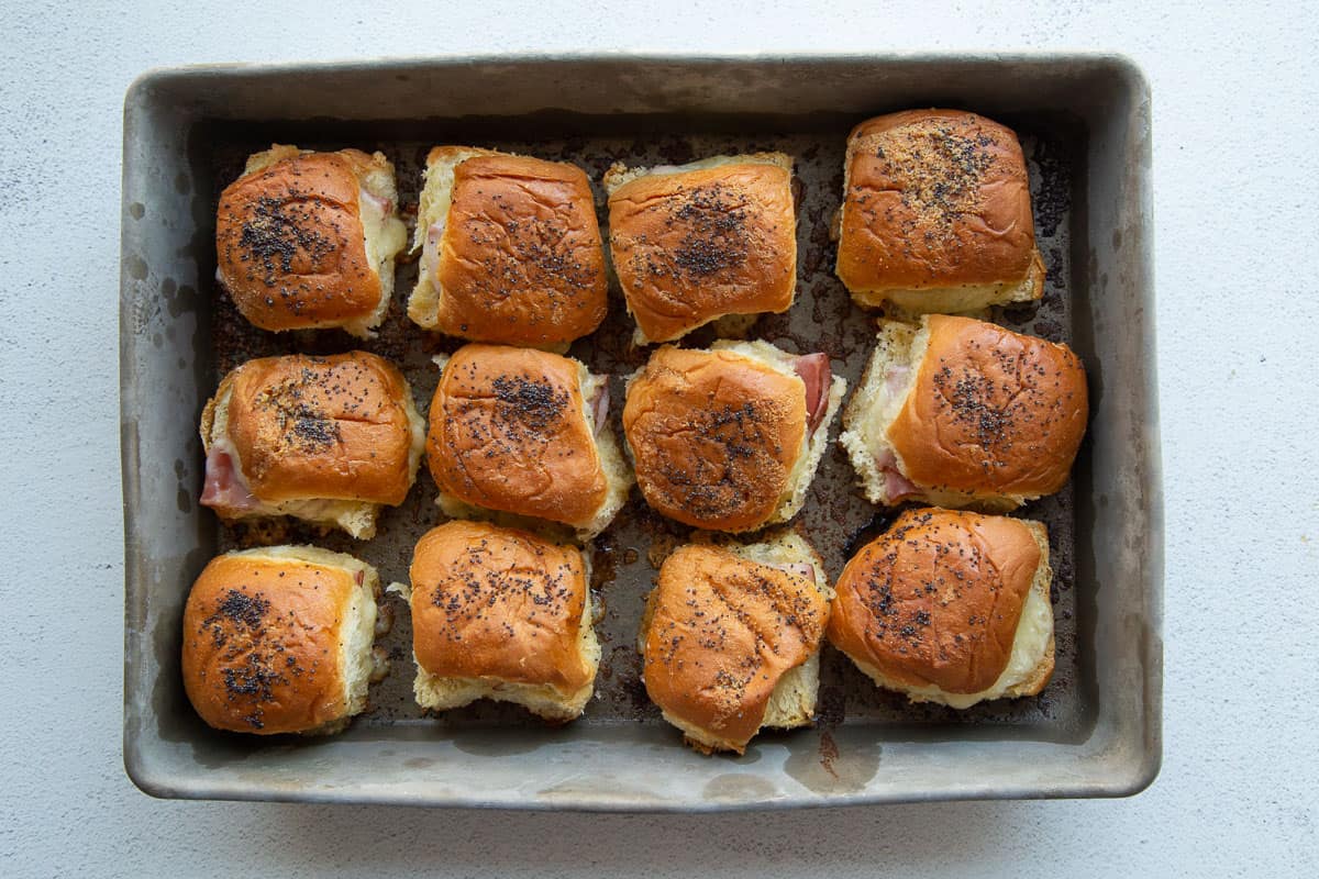 ham and cheese sandwiches on hawaiian buns in a metal baking dish.