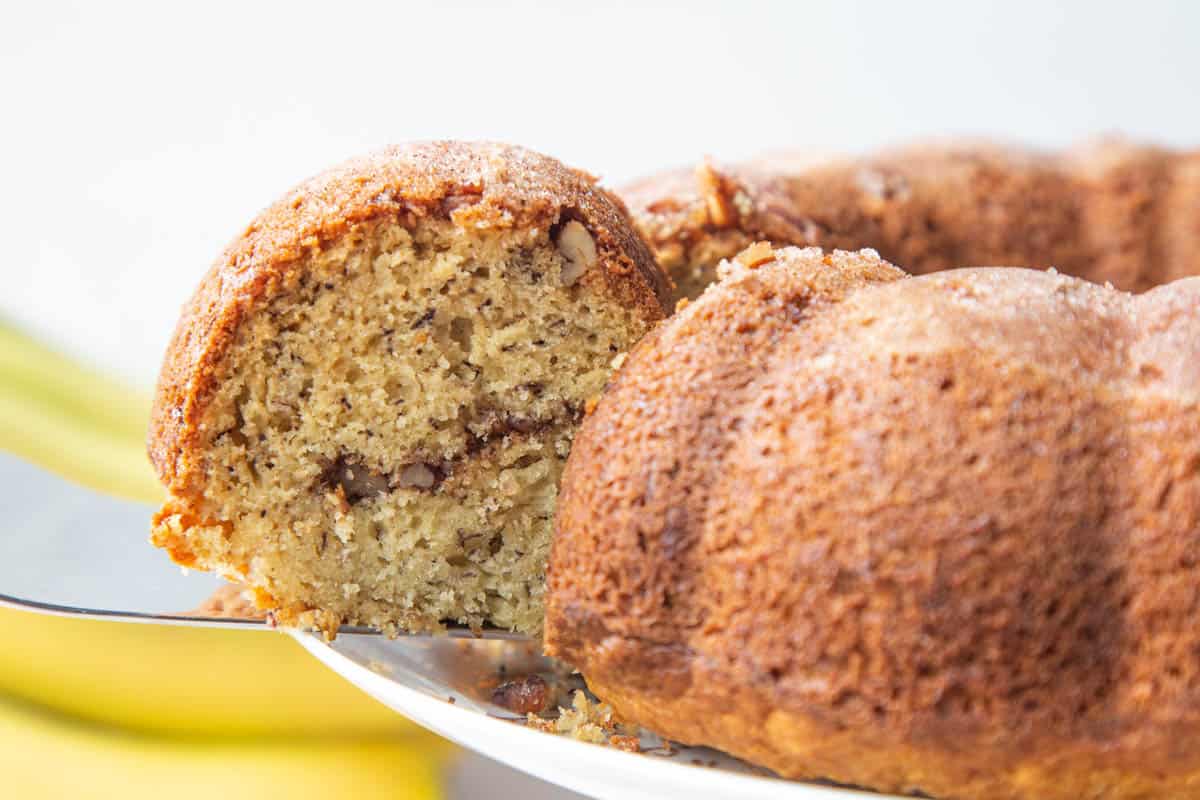 silver serving utensil pulling a slice of banana coffee cake out of a whole coffee cake.