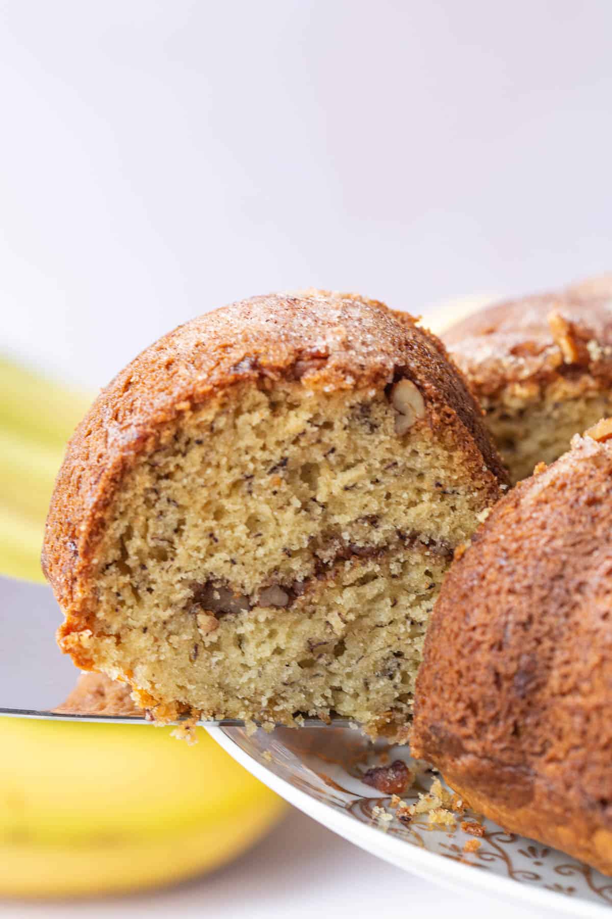 silver serving utensil pulling a slice of banana coffee cake off of a cake stand.