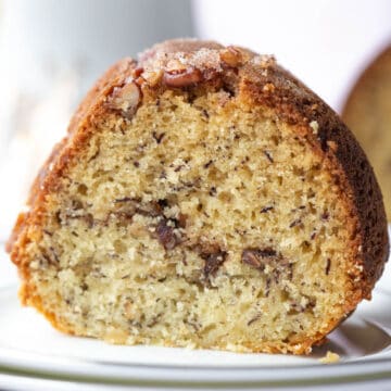 slice of banana coffee cake with pecan streusel in the middle on a white plate.