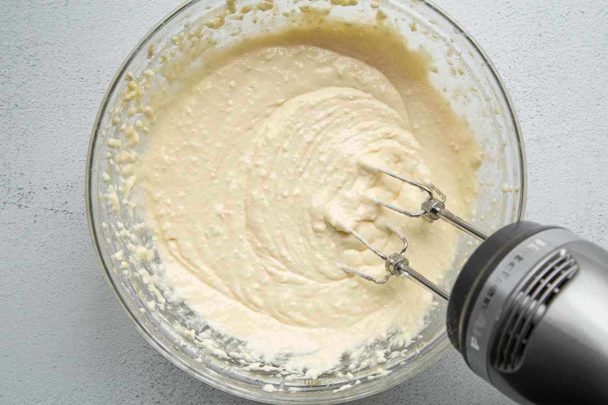 hand mixer mixing a cream cheese mixture in a glass bowl.