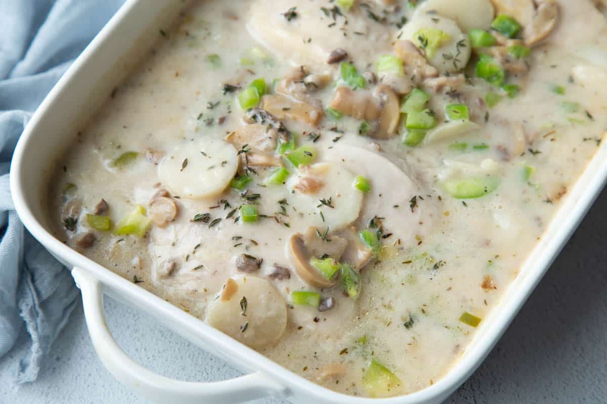 white casserole dish filled with cream of mushroom chicken, diced peppers, and sliced mushrooms.