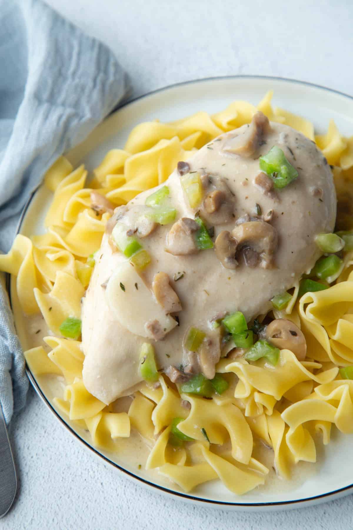 cream of mushroom sauce on top of a chicken breast, on top of egg noodles on a white plate.