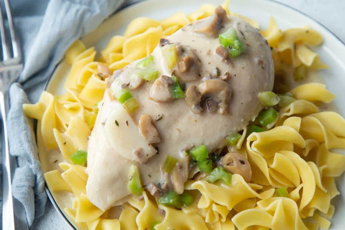 chicken breast and cream of mushroom sauce over egg noodles on a white plate.