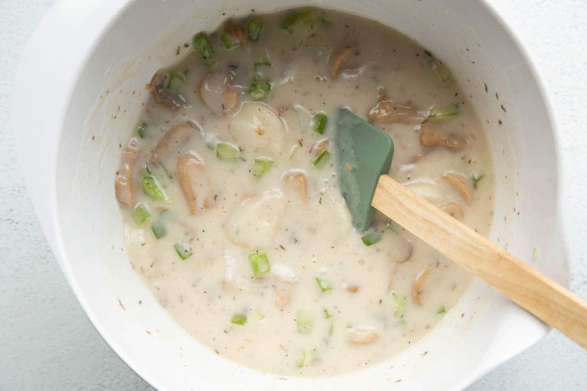 diced green peppers and cream of mushroom soup in a white bowl with a green wooden spatula.