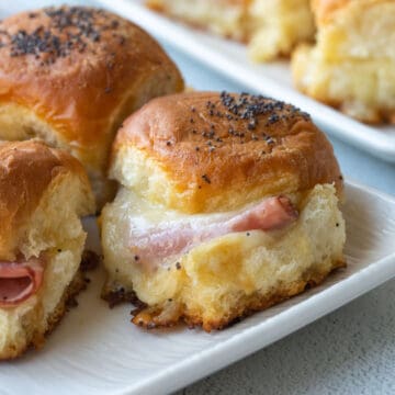 ham and cheese mini sandwiches on hawaiian rolls, topped with poppy seeds, on a white platter.