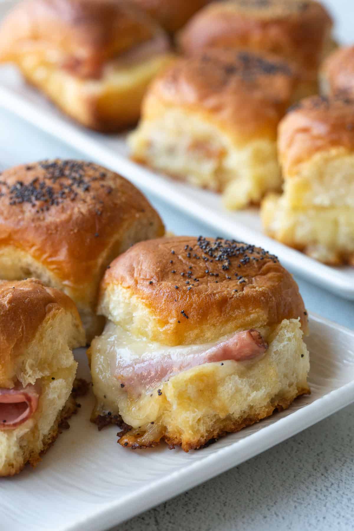 hawaiian roll sliders with ham and cheese on two white platters.