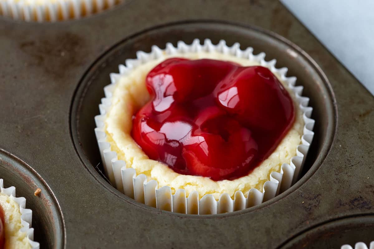 mini cheesecake topped with cherry pie filling in a muffin tin.