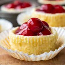 mini cheesecake topped with cherries in a white muffin cup liner.