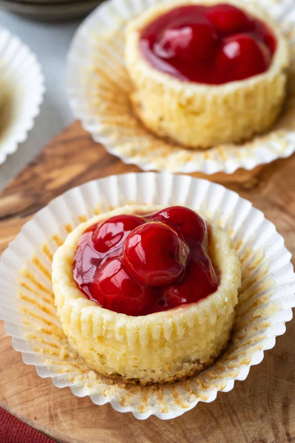 mini cherry cheesecake in a white cupcake liner on a wooden board.