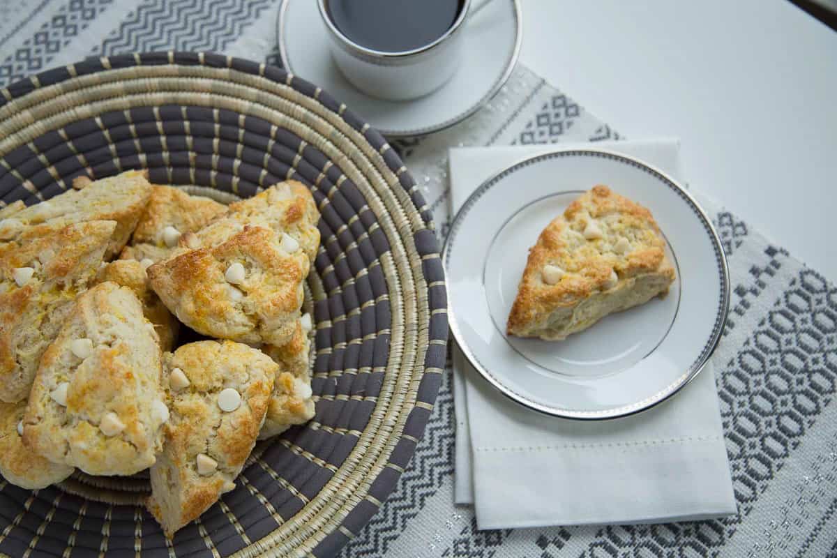 orange scones in a decorative basket and on e white plate, next to a cup of coffee.