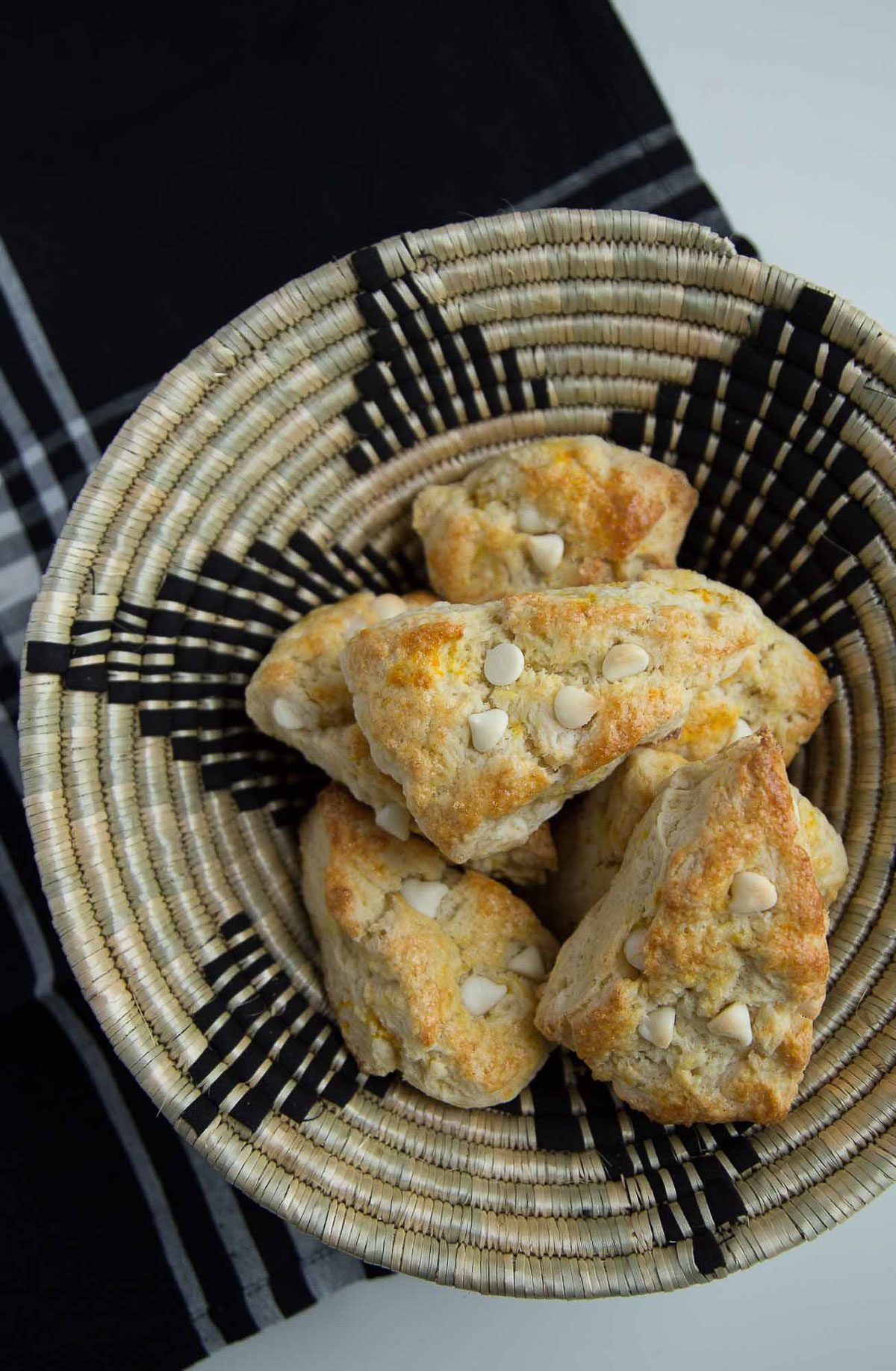 orange scones with white chocolate chips in a decorative woven basket.