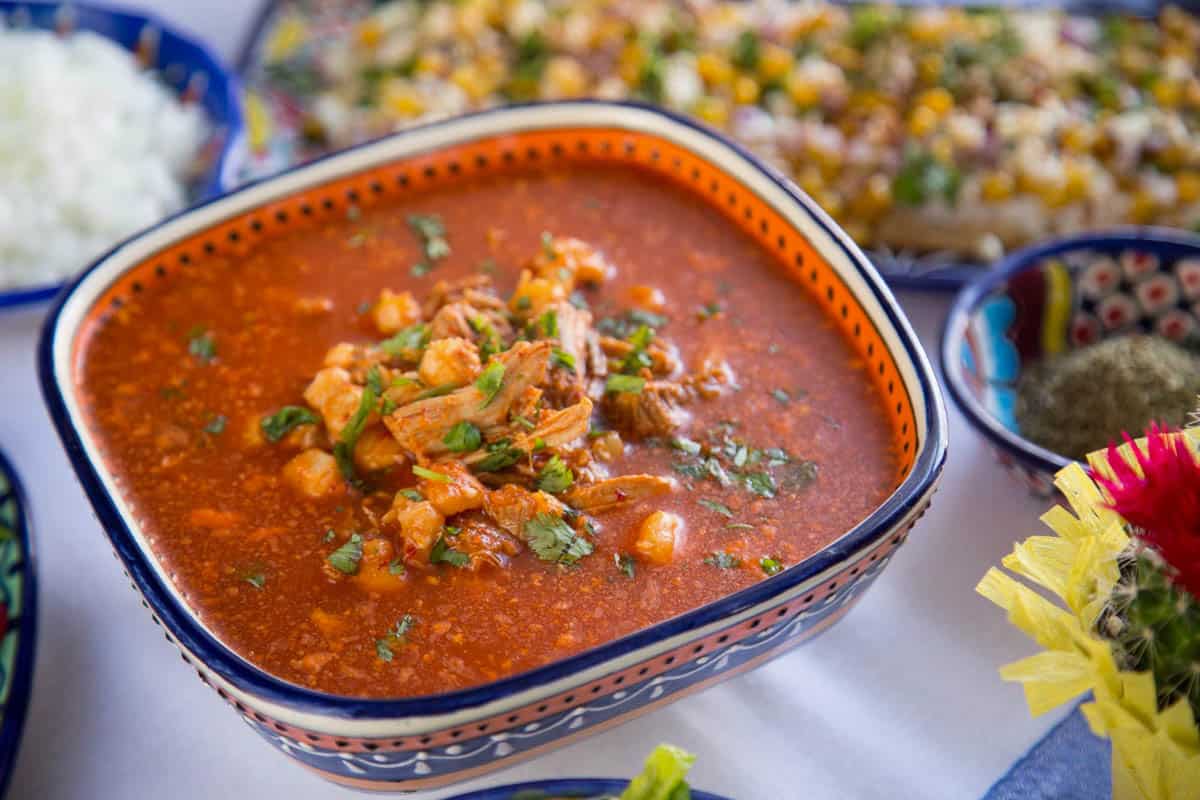 decorative bowl filled with red pozole, topped with chopped cilantro.