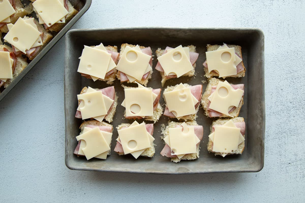 rolls topped with ham and cheese in a metal pan.