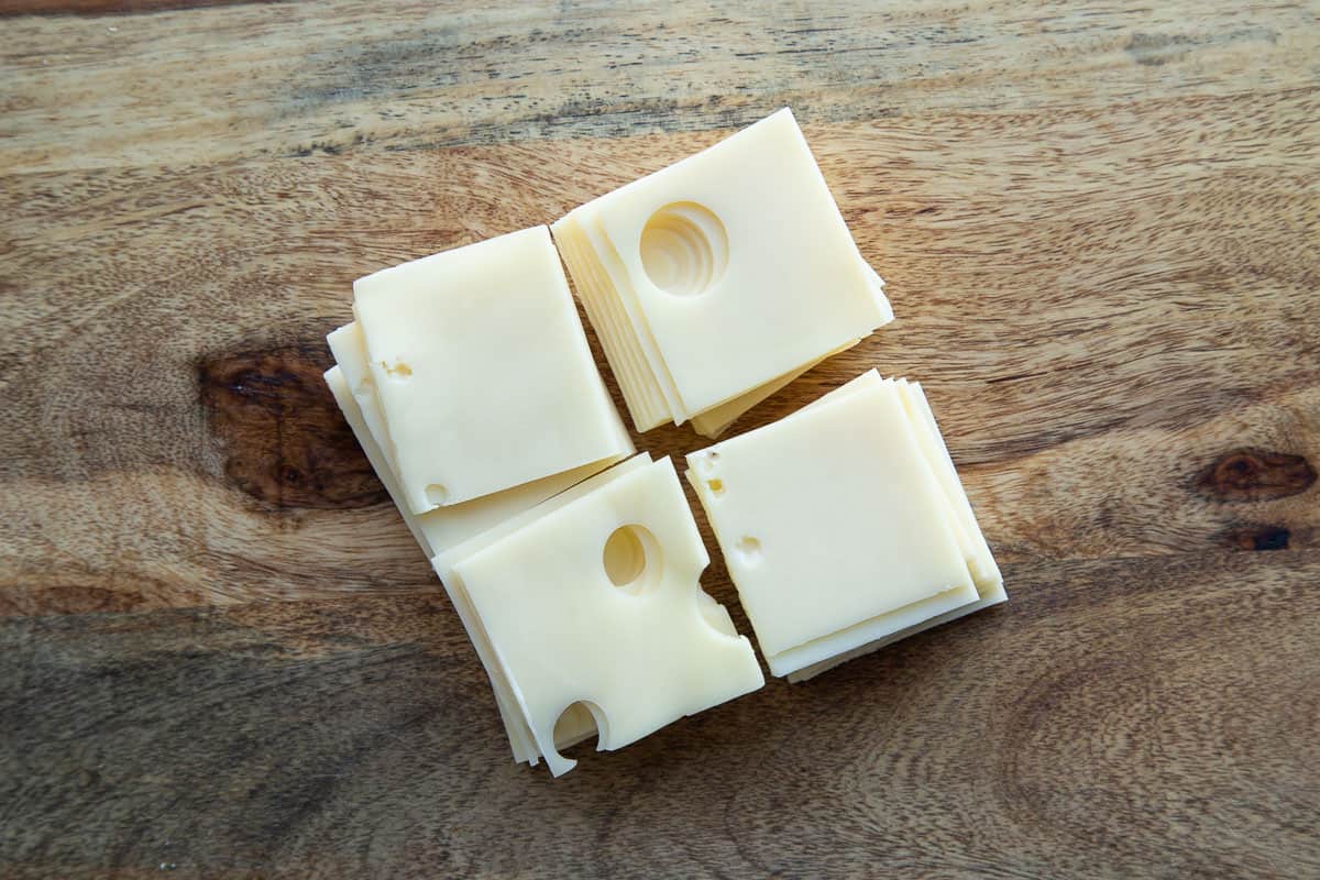 slices of swiss cheese cut into quarters on a wooden cutting board.