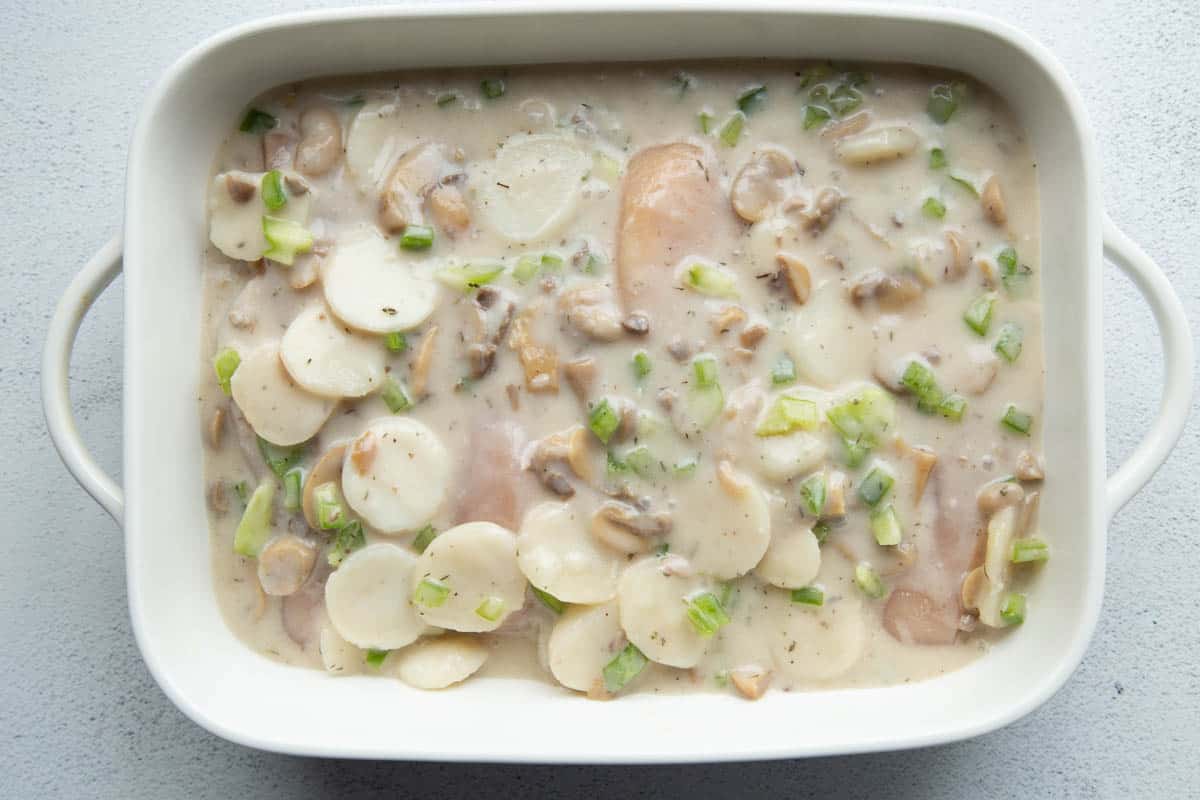 chicken breasts topped with water chestnuts and green pepper pieces in a creamy sauce, in a white casserole dish.