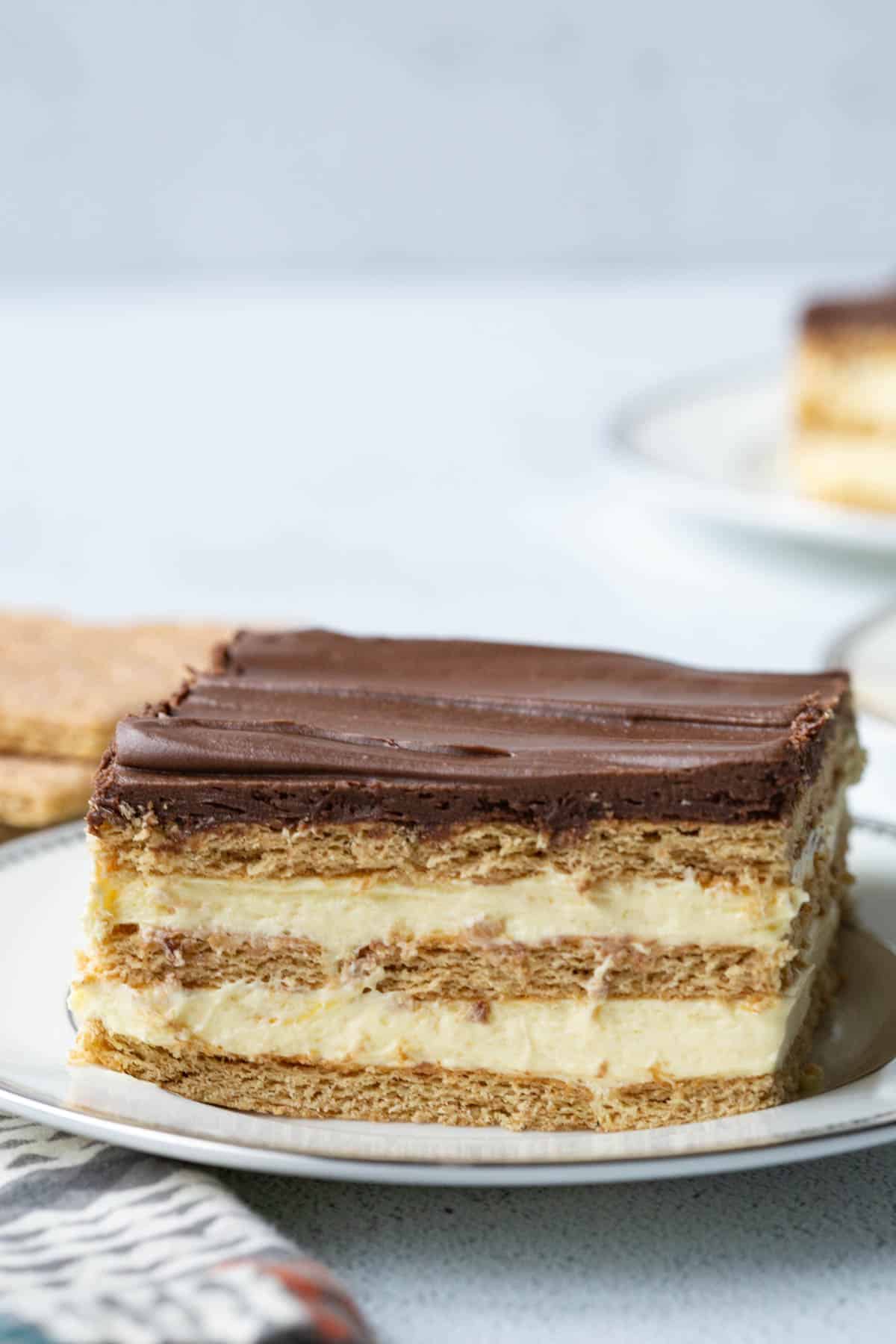 layered chocolate eclair cake with chocolate frosting on a white plate.