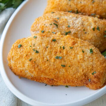 baked parmesan crusted chicken breasts on a white platter.