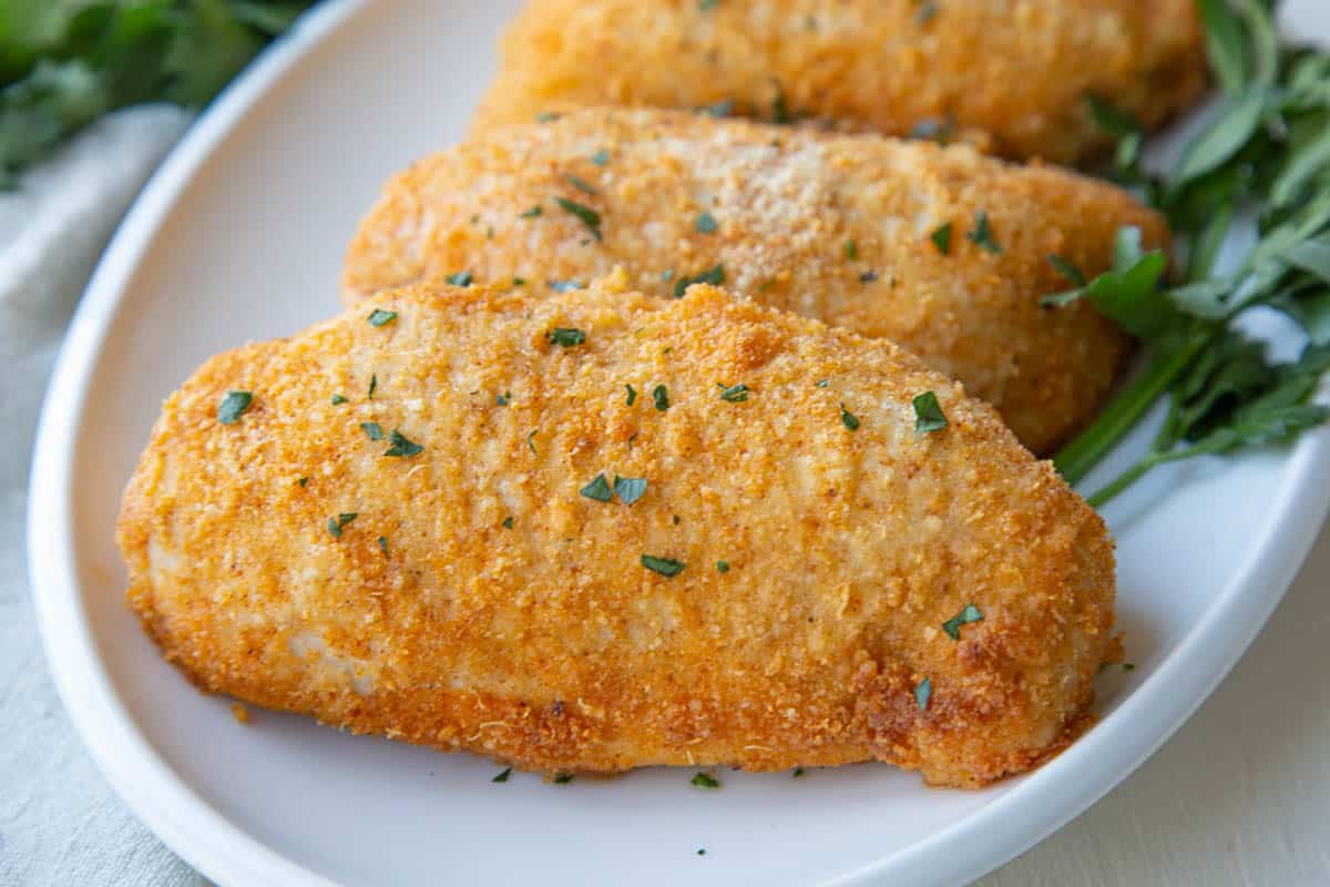 baked chicken breasts topped with breadcrumbs and parmesan on a white platter.