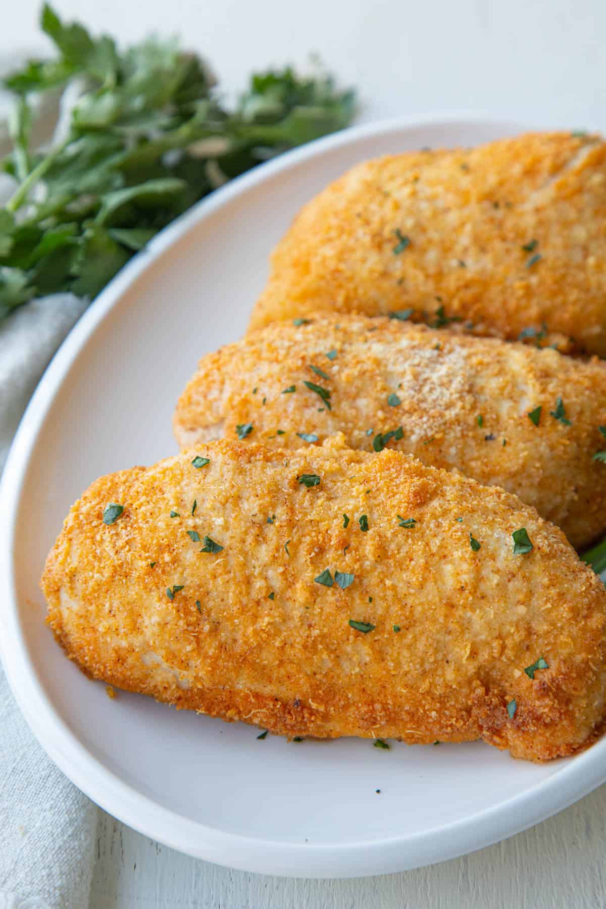 baked parmesan crusted chicken breasts on a white platter.